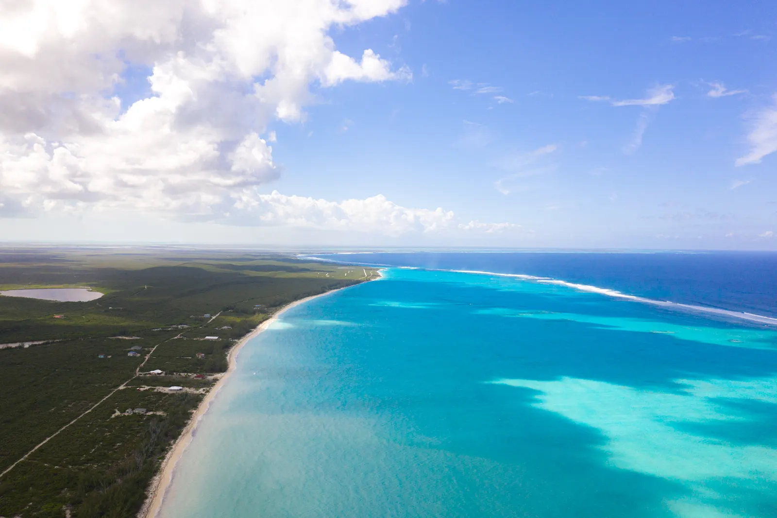 A long white beach and turquoise shallows running out to the reef, green scrub inland, seen from the air