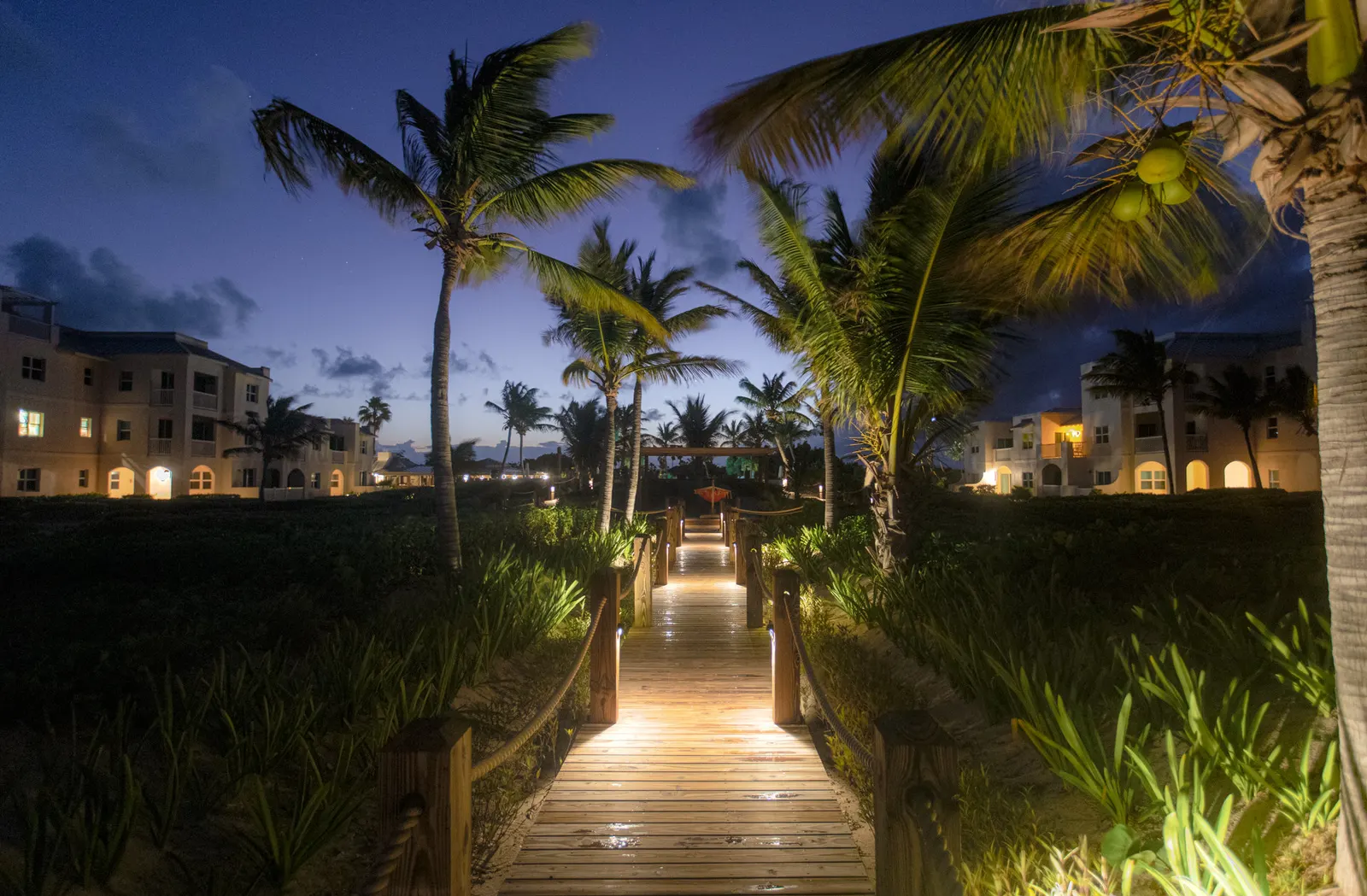 The resort's lit boardwalk between the low white buildings at dusk